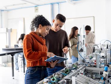 Team of robotic students using a digital tablet while operating a production line robot - STEM education concepts